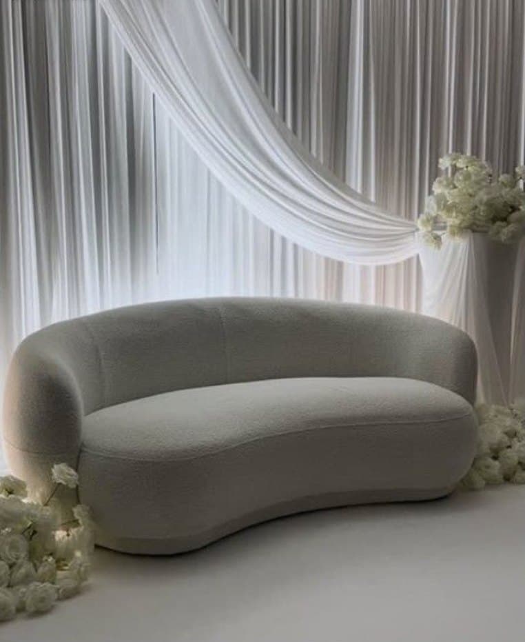 Trône des mariés en tissu bouclé blanc devant un fond de voilages et de fleurs